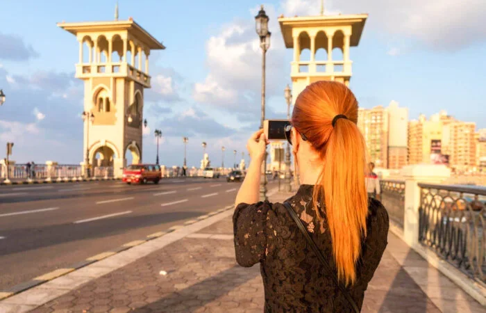 A woman with red hair photographing the twin towers of Stanley Bridge with her phone during golden hour.