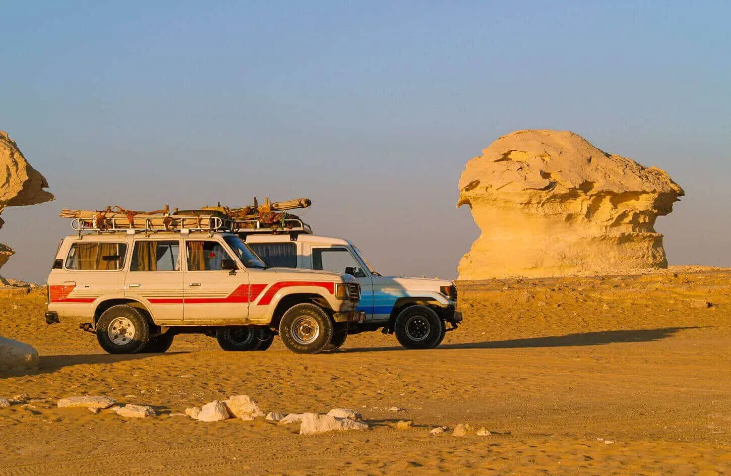 A white 4x4 Land Cruiser is parked in front of a large mushroom-shaped white chalk rock formation.