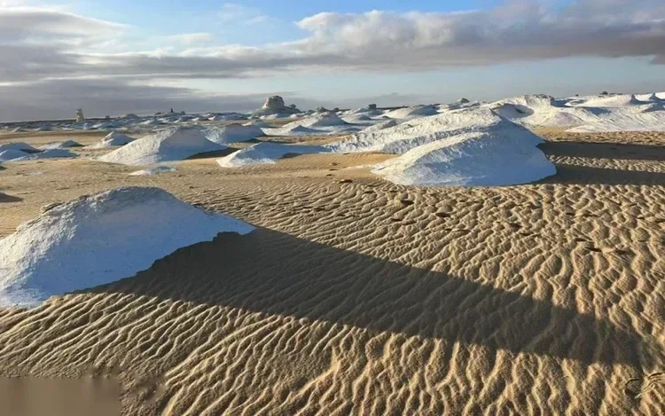 Schneeweiße Mineralhügel auf gewellten Sanddünen unter leicht bewölktem Himmel zur goldenen Stunde