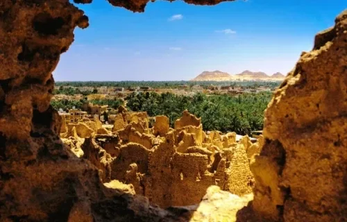 Blick durch eine Felsöffnung auf die grünen Palmenhaine der Oase Bahariya mit Wüstenhügeln dahinter