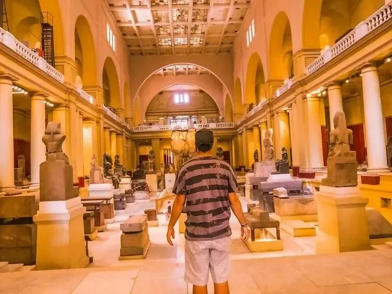 Férfi sétál az Egyiptomi Múzeum Nagy Csarnokában, nagy gránitszobrok és kőszarkofágok között