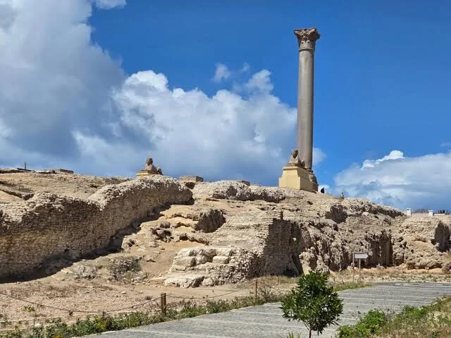 Широкий вид на археологический участок колонны Помпея: колонна и небольшая статуя сфинкса над раскопанными руинами