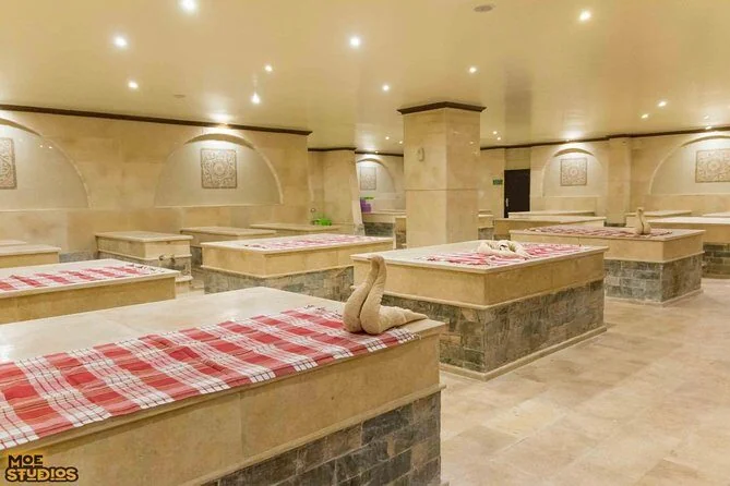 An empty hammam-style spa room with stone benches topped in red-and-white checkered towels folded into swan shapes
