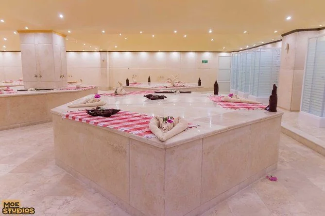 Leerer Hammam-Spa-Raum mit Steinbänken, rot-weiß karierte Handtücher zu Schwänen gefaltet, Deckenspots
