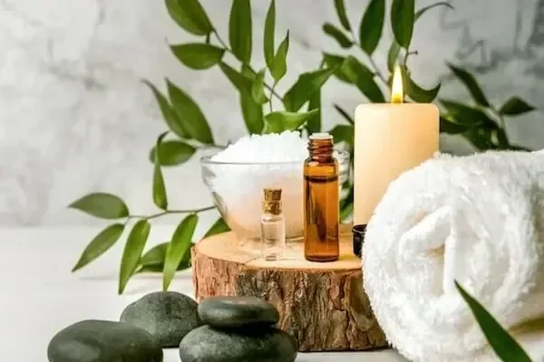 A spa still-life of bath salts in a glass bowl, small amber oil bottles, a lit candle, black hot stones