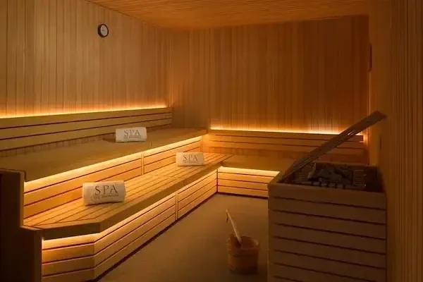 A wood-paneled sauna room with illuminated tiered benches holding folded towels labeled SPA