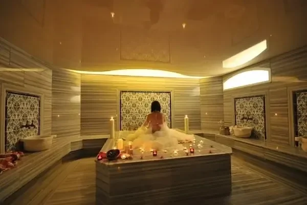 A woman sits on a marble platform covered in bath foam, seen from behind
