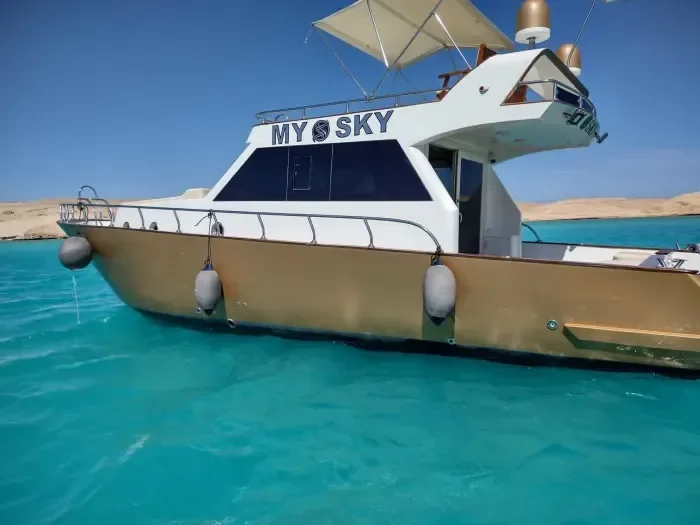 The gold-hulled yacht My Sky floating at anchor in turquoise water near a sandy Red Sea island.