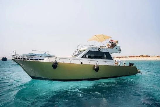 Full side view of the My Sky yacht anchored offshore, showing its shaded upper deck and gold-and-white hull.