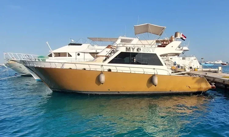 The My Sky yacht moored at a dock with its gold hull and Egyptian flag visible, other boats in the background.
