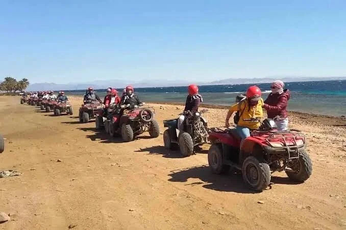 Pilotes de quad en casques rouges roulant en file indienne sur une piste sablonneuse le long du littoral de la mer Rouge