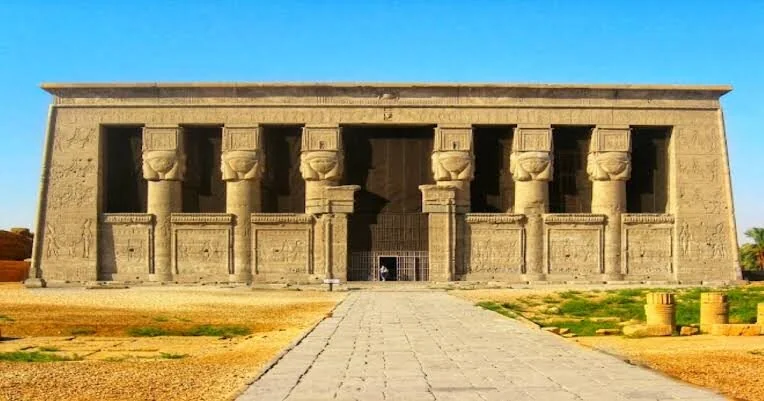 Scattered stone column fragments and ruins lie in the courtyard in front of Dendera Temple's facade.