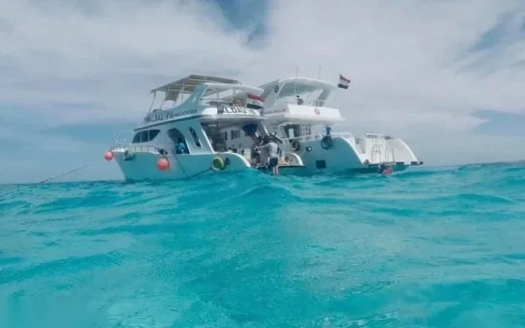 Two catamaran-style dive boats anchored side by side in turquoise water under a cloudy sky.