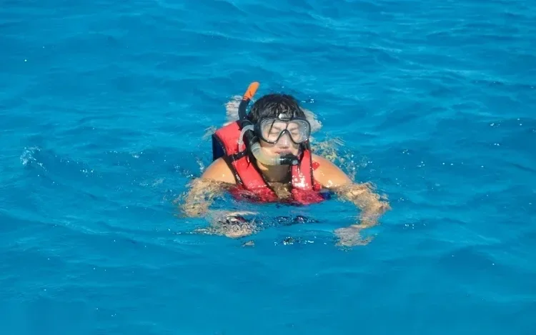 Snorkeler in an orange life vest and mask swimming at the surface.
