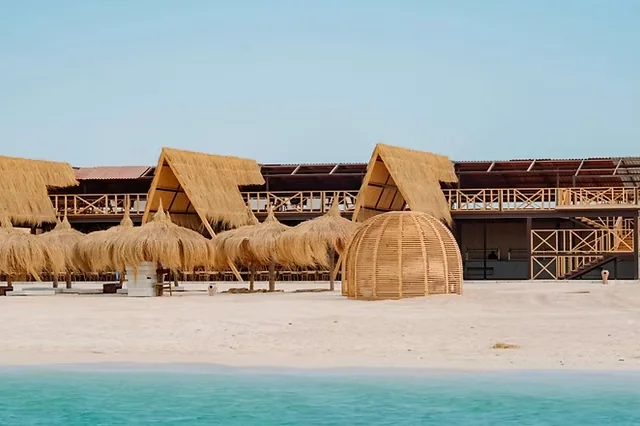 Rij strandcabana's met rieten dak en een koepelvormige rieten hut op wit zand naast turquoise water