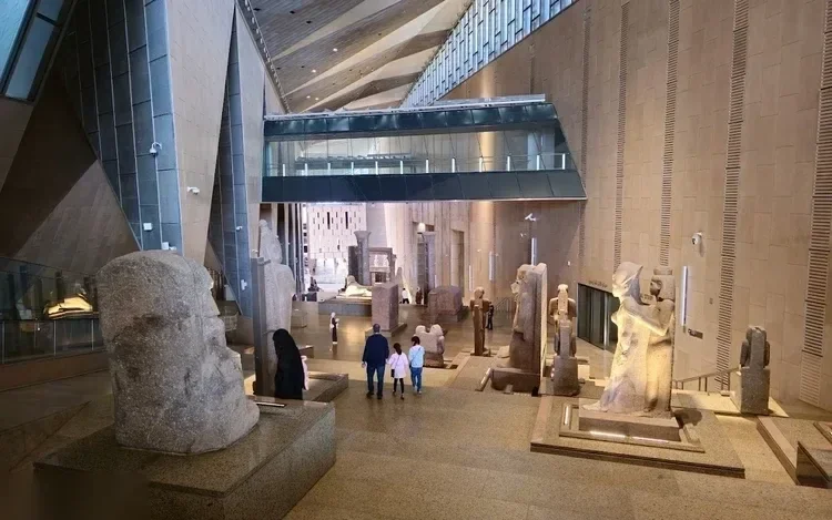 大埃及博物馆的大厅，成排的古代石像，游客从旁走过
