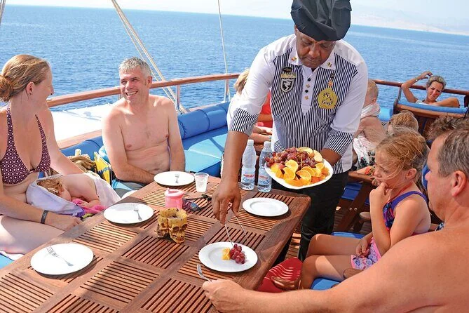 Steward en uniforme servant un plateau de fruits frais à une famille attablée à une table extérieure du yacht