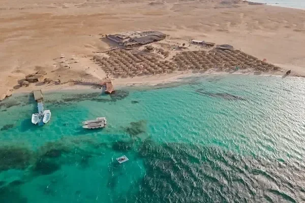 Vue aérienne d'une île-plage privée avec parasols de paille, ponton et bateaux ancrés en eau turquoise