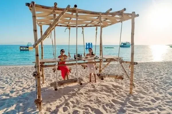 Couple assis à une table-balançoire en bambou sur le sable blanc au bord de la mer au coucher du soleil