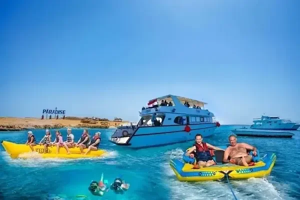 Légifelvétel egy banánhajóról és egy utasokkal teli vontatható tubusról egy kikötött hajó és a Paradise-sziget tábla
