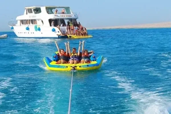 Négytagú család egy sárga felfújható vontathatón felemelt karokkal ujjong, a háttérben a Sea Wind hajóval
