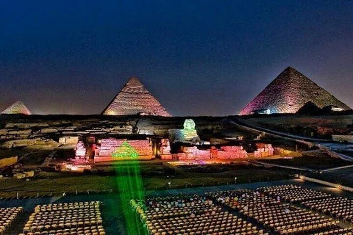 لقطة ليلية قريبة لهرمين مضاءين بالألوان البرتقالية والخضراء، وأبو الهول مضاء بينهما