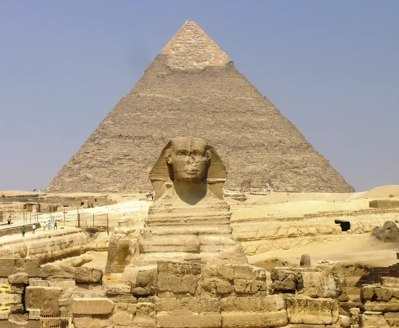 Front view of the Great Sphinx of Giza with the Pyramid of Khafre rising directly behind it against a clear sky.
