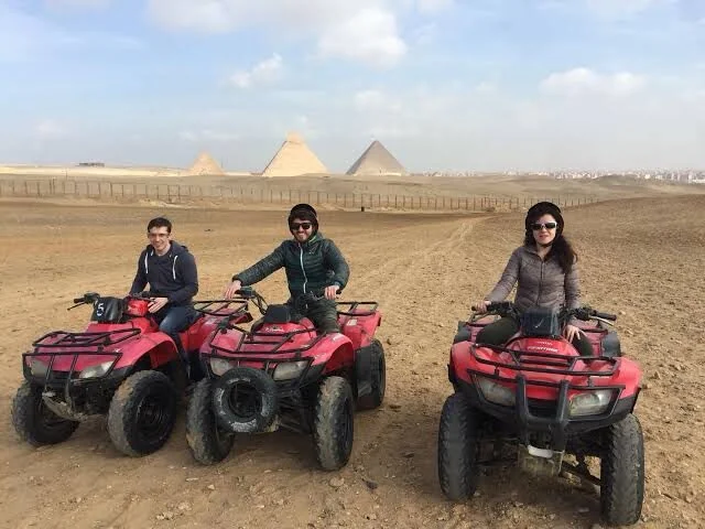 Drie rijders op rode quads poseren voor een foto met enkele piramides van Gizeh op een rij op de achtergrond