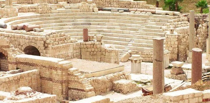 منظر مرتفع للمدرجات الحجرية المنحنية للمدرج الروماني، تحيط بها آثار من الطوب والحجر منقّب عنها