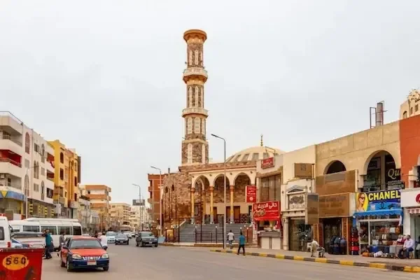Straße in der Innenstadt von Hurghada mit hohem verziertem Minarett, Geschäften und vorbeifahrendem Verkehr