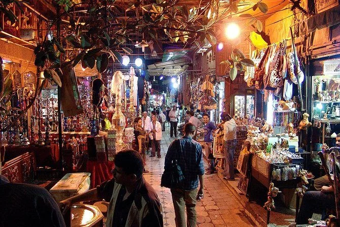 Ruelle de marché de nuit ornée de lanternes et de narguilés, des clients parcourant les étals
