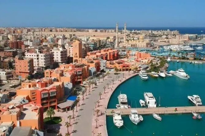 Vue aérienne de jour de la marina de Hurghada : immeubles orange, promenade bordée de palmiers et yachts à quai