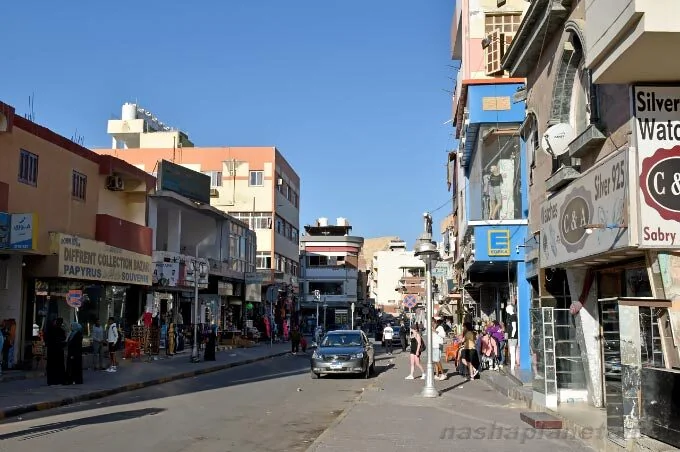 Rue ensoleillée du centre de Hurghada bordée de boutiques, dont l'enseigne d'un magasin Silver Watch, des piétons marchant