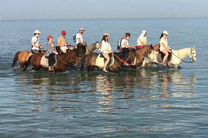 A line of riders on horseback walking through shallow turquoise sea water off a Hurghada beach.