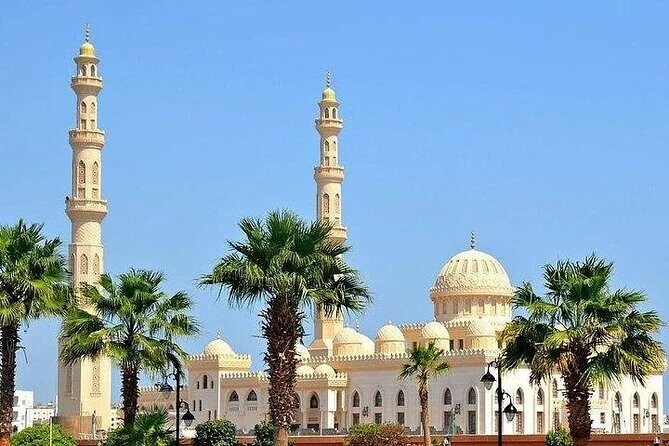 Grande mosquée blanche à deux hauts minarets et dôme central, entourée de palmiers sous un ciel bleu dégagé