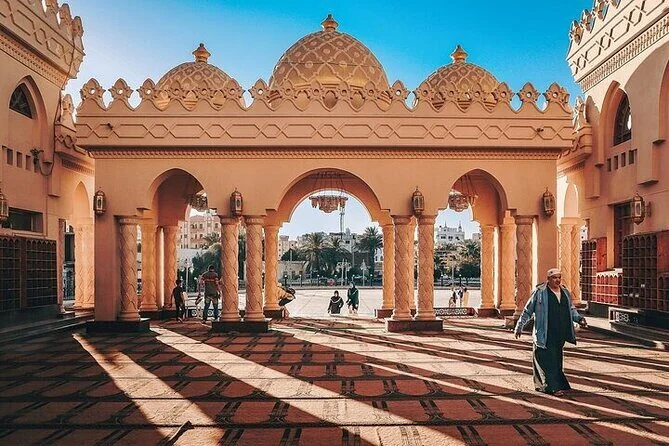 Arche ornée à plafond en dôme et colonnes sculptées ouvrant sur une cour, un homme en tenue traditionnelle passant