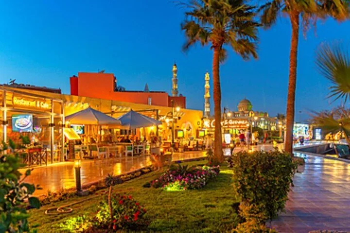 Restaurantterrasse im Freien mit Schirmen und Palmen in der Dämmerung, im Hintergrund beleuchtete Minarette