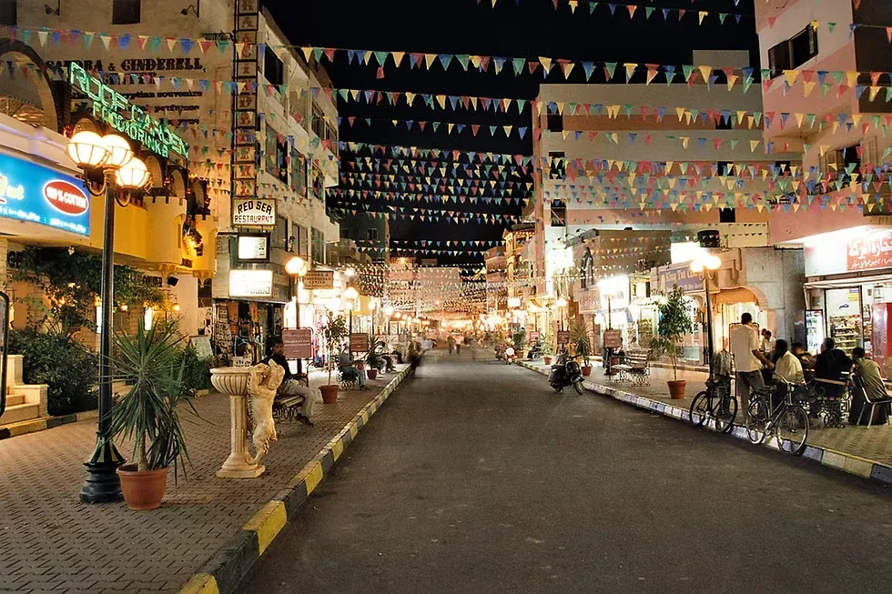 شارع تسوق مضاء بأجواء احتفالية ليلًا تعلّق فيه رايات مثلثة ملونة فوق المحال ومطعم
