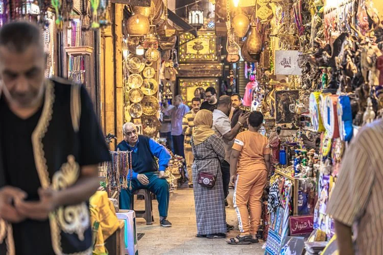 ممر بازار مغطى مزدحم مليء بالفوانيس والمجوهرات والهدايا التذكارية، ومتسوقون وباعة يتفاعلون