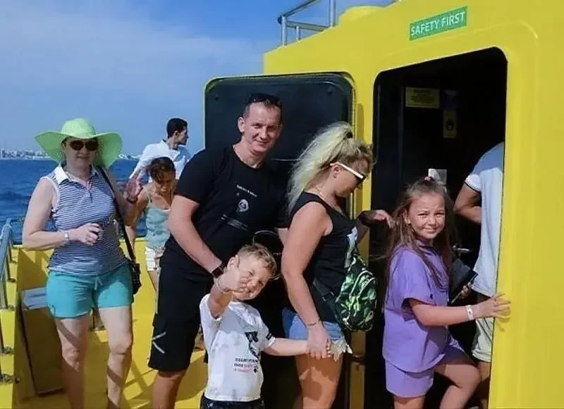 Familie mit zwei Kindern posiert an der gelben Einstiegsluke des Halbtauchboots mit der Aufschrift Safety First