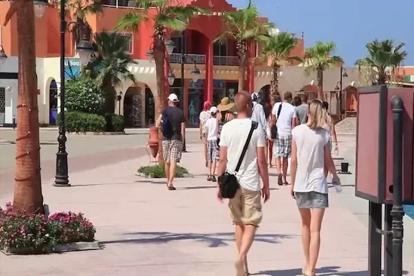 سياح يمشون على ممشى للمشاة تصطف عليه النخيل، مارّين بمبانٍ حمراء وبرتقالية على الطراز الاستعماري