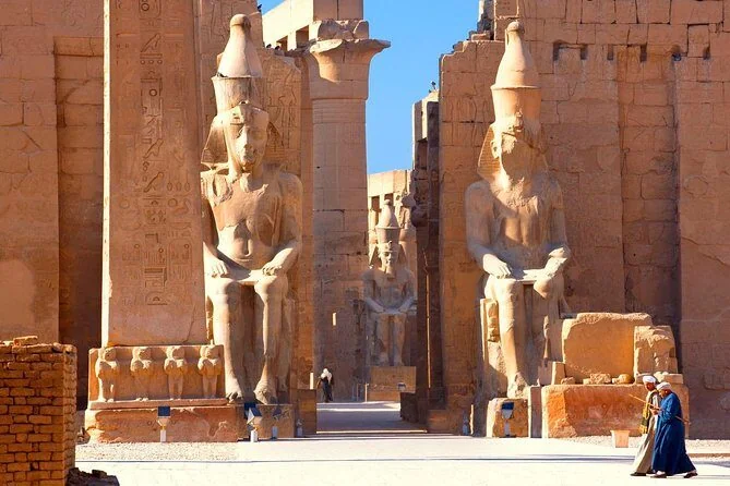 Twee kolossale zittende farao-beelden flankeren een tempelpoort van de Luxortempel terwijl twee mannen in traditionele