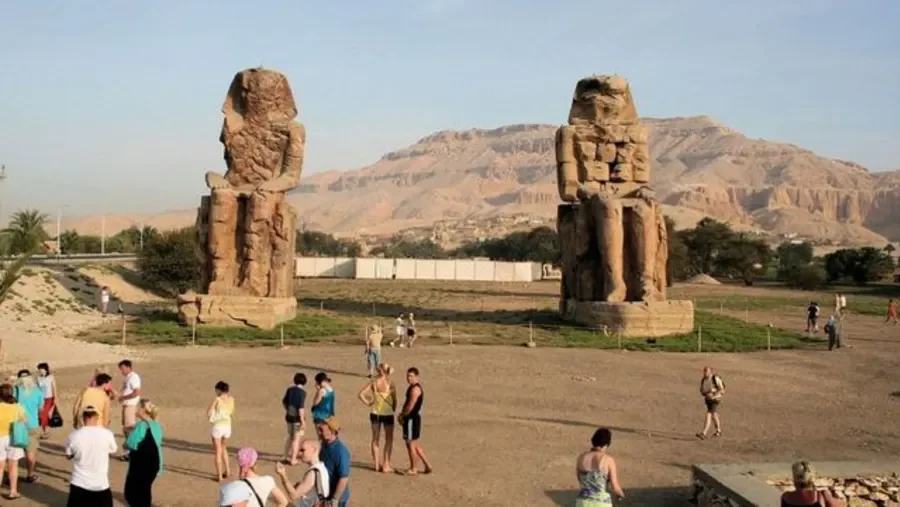 De twee zittende Colossi van Memnon rijzen op uit de woestijnvlakte met de heuvels van Thebe op de achtergrond