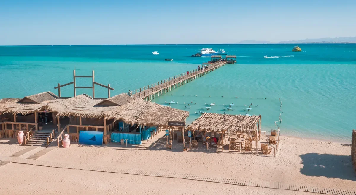 Aerial view of Orange Bay's wooden pier stretching over turquoise water to a straw-roofed beach lounge
