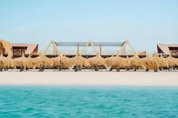 صف من أكواخ الشاطئ بسقف من القش يُرى من الماء والبحر الفيروزي في المقدمة