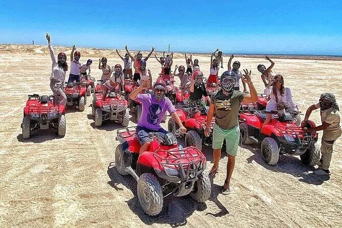 مجموعة كبيرة من الراكبين بخوذات يلتقطون صورة على دراجات رباعية حمراء مصطفة في الصحراء رافعين أذرعهم