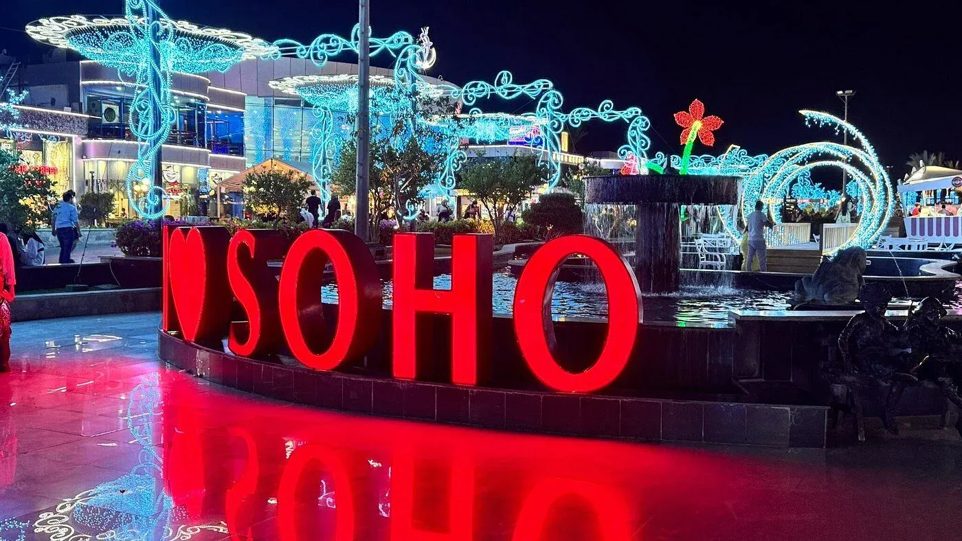 Kivilágított vörös „I Love Soho” felirat egy szökőkút mellett a sarm el-sejki Soho Square-en éjjel