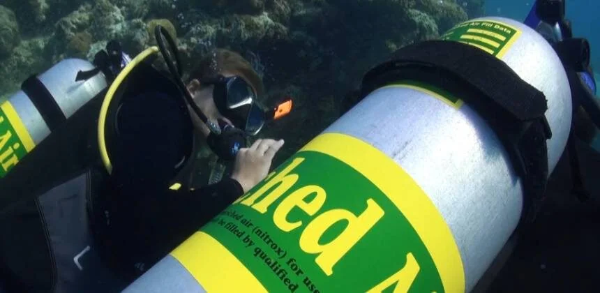 Gros plan sous-marin d'un plongeur lisant l'étiquette jaune et verte Enriched Air Nitrox sur une bouteille