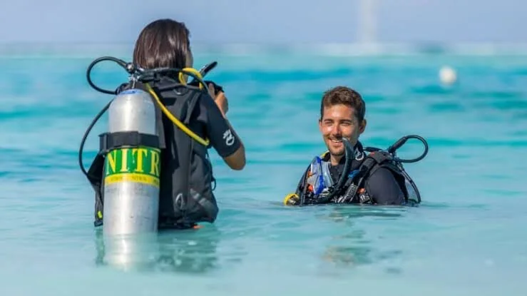 Deux plongeurs dans l'eau peu profonde, l'un portant une bouteille NITROX, bavardant et se souriant