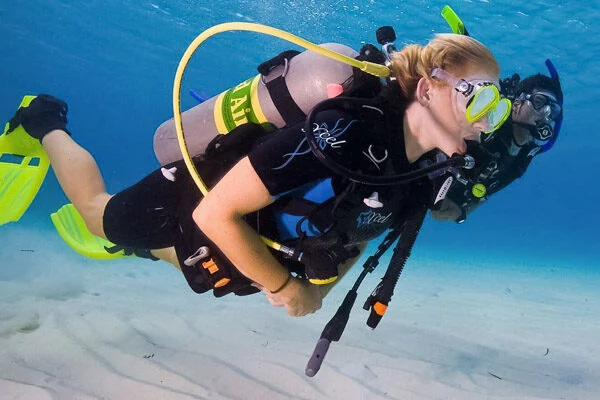 Deux plongeurs côte à côte sous l'eau, l'un avec une bouteille Nitrox à étiquette jaune, au-dessus d'un fond sableux